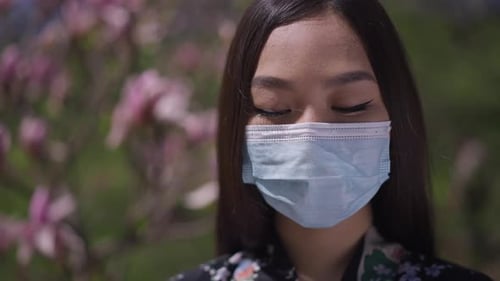 Closeup Portrait of Asian Young Woman in Coronavirus Face Mask Opening Eyes Looking at Camera