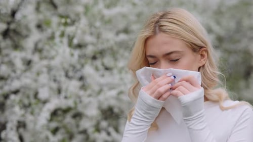 Sick Woman Blowing Runny Nose in Tissue During Walk in Park