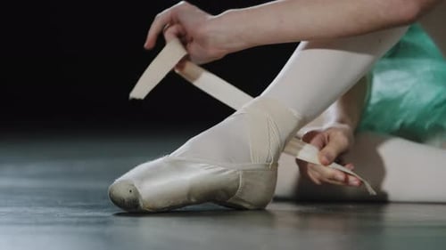 Ballerina Tying Pointe Shoe on Dark Stage