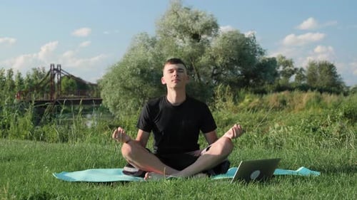 Man Meditating Outdoors Near Laptop on Sunny Day