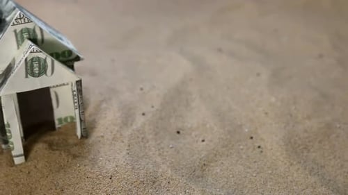 House Cut Out of Dollar Bills on the Sand