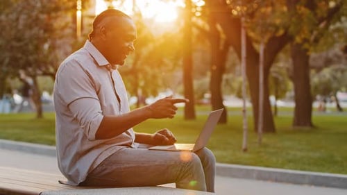 Man Using Laptop in Park at Sunset
