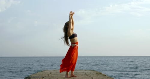 Long Haired Brunette Dances on Asphalt Pier Against Blue Sea