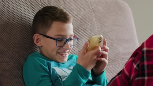 Smiling Boy Using a Smartphone on Couch Indoors