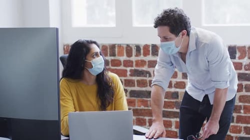Homme et femme portant des masques faciaux travaillant ensemble au bureau