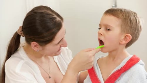 Woman Helping Young Child Brush Teeth in Bathroom