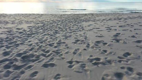 AERIAL: Pan Shot of Sandy Beach Filled with Foot Prints and Human Tracks with Sea