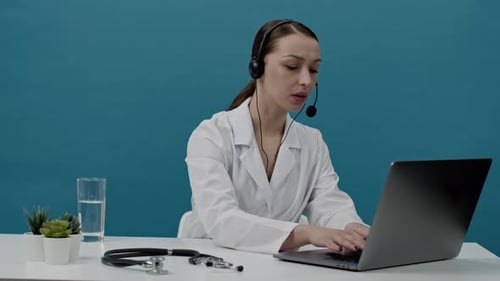 Female Doctor in White Coat Using Laptop and Headset