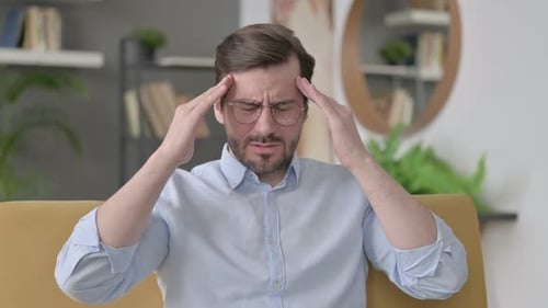 Man Experiencing a Headache Rubbing Temples on Couch