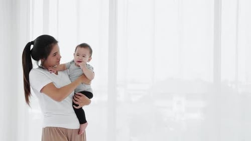 Woman Holding Cute Baby Near Window at Home