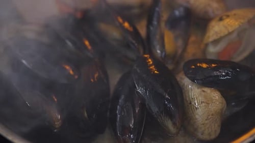 Cuisson des moules et des pétoncles dans une poêle avec du bouillon