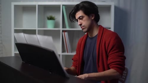 Side view of handsome young musician man playing piano at home studio during lesson in free time.
