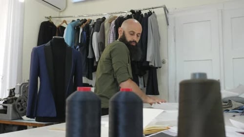 Bearded Tailor Arranging Garment Patterns in Bright Workshop