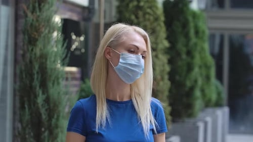 Woman Puts On Surgical Mask in Urban Setting