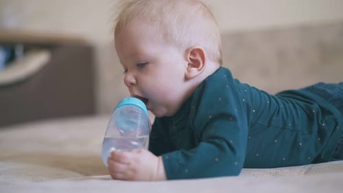 Adorable Boy Nibbles Bottle Teat Lying on Soft Bed in Room