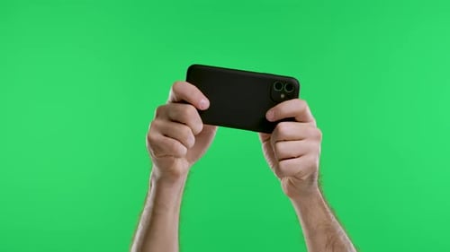 Male Hands Hold a Smartphone Horizontally Against the Background of a Green Screen Chroma Key