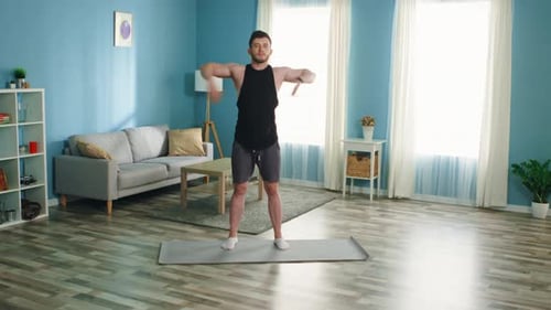 Man Doing Arm Rotations on a Yoga Mat Indoors