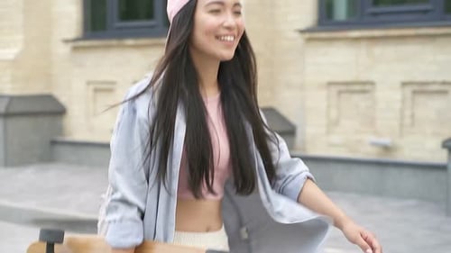 Young Woman Smiling and Carrying Skateboard Down Street