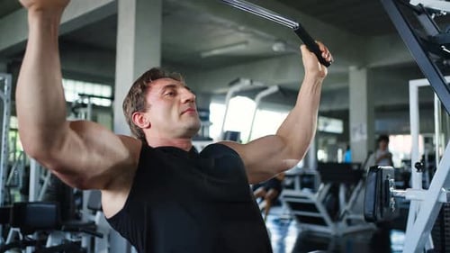 4K Caucasian man bodybuilder pulling weight lifting machine at gym.