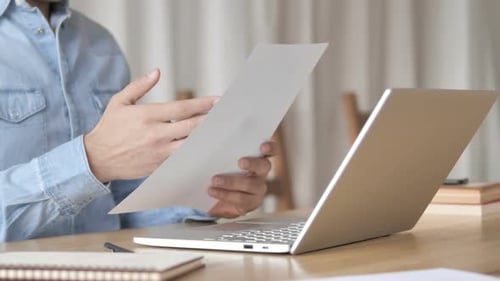 Person crumples paper at desk with laptop