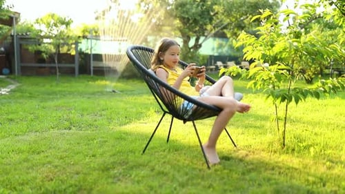 Happy kid girl playing game on mobile phone in the park outdoor