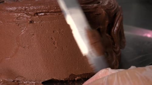 Chocolate Frosting Is Spread Over the Side of a Dark Cake Base with a Knife - Closeup