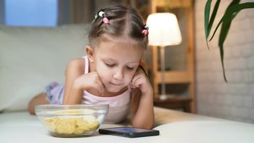 Girl Lying on Couch Watching Phone Eating Chips