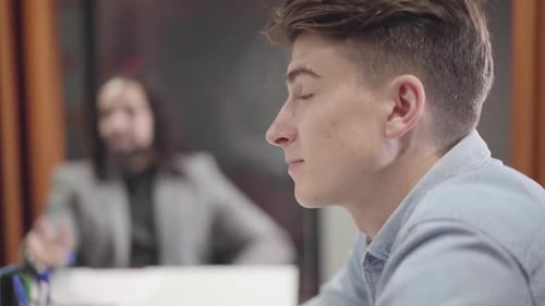 Side View Close-up of Young Caucasian Man Sitting with Coworkers at the Table and Discussing Ideas