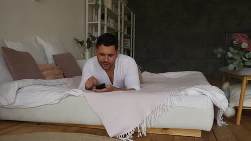 Man Using Smartphone Relaxing on Bed at Home