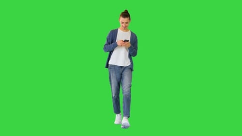 Young White Man Walks Typing Something on His Smartphone on a Green Screen Chroma Key