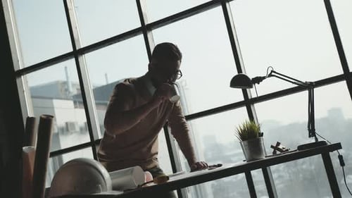 Engineer Works in a Bright Office with a Large Window, Concentrates
