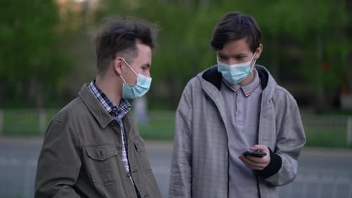 Zwei Freunde in medizinischen Masken sprechen, wenn sie sich im Freien treffen