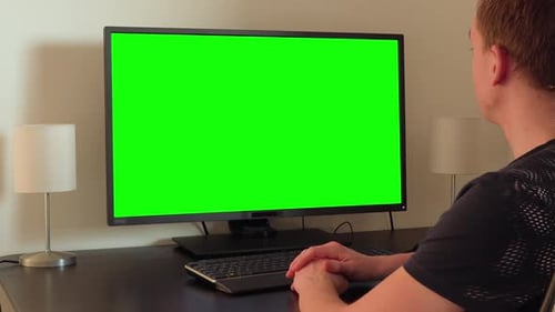 Ein Mann sitzt an einem Tisch und schaut auf einen grünen Computerbildschirm