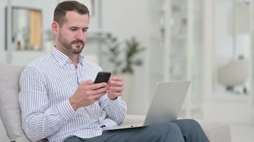 Man Using Laptop and Mobile Phone on Couch