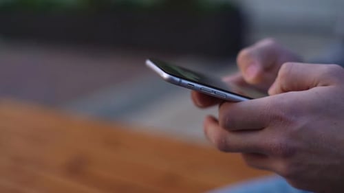 Close-up hands of business man typing message on mobile phone outdoors at city street.