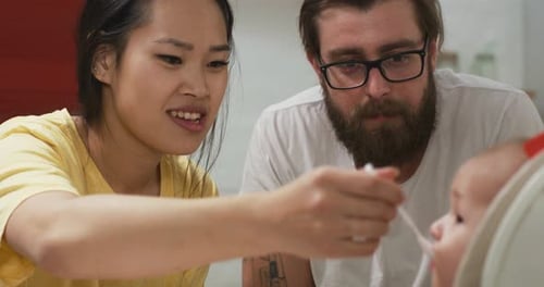 Parents Feeding Infant in High Chair Indoors