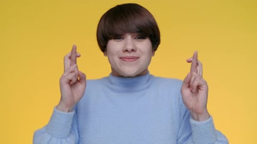 Woman Crossing Fingers in Front of Yellow Background