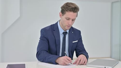 Serious Young Businessman Doing Paperwork in Office