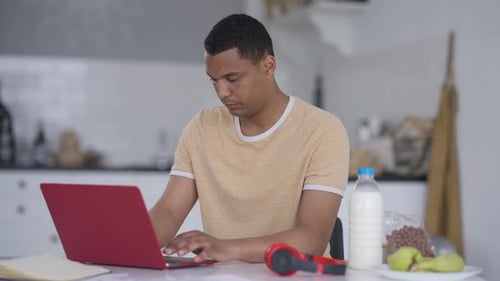 Retrato de un hombre concentrado sentado en la mesa de la cocina escribiendo en el teclado del ordenador portátil en cámara lenta