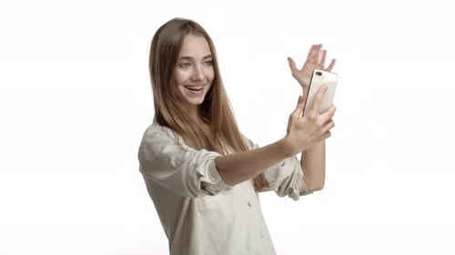 Studio Shot of Attractive Blond Woman with Braces on Her Teeth Talking on Video Call Holding Mobile