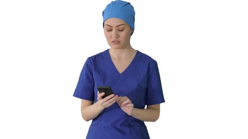Female Doctor or Nurse in Blue Uniform Using Her Phone As She Walks on White Background