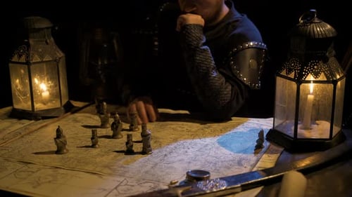 Man Strategizing with Chess Pieces on Map by Lantern