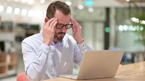 Stressed Businessman with Laptop Having Headache in Office