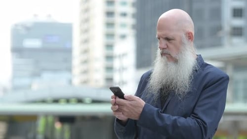 Happy Mature Bearded Bald Businessman Talking on the Phone in the City Outdoors