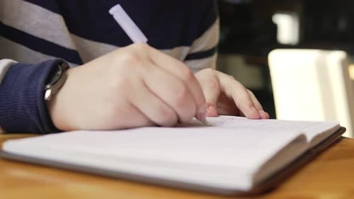 Closeup View of Male Hand Writing in His Notebook Sitting at the Table