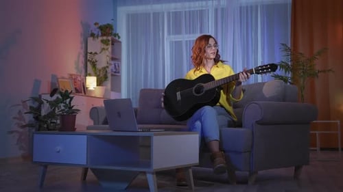 Woman Plays Guitar on Couch at Night
