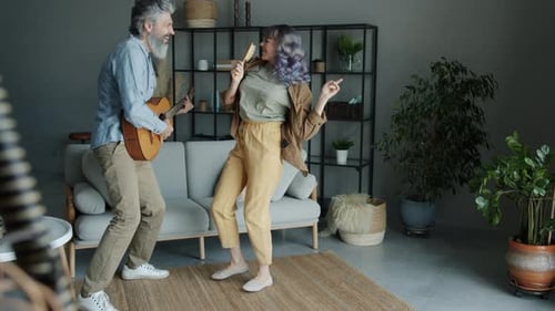 Joyful Couple Dancing and Singing Playing the Guitar Then Kissing Having Fun Indoors in Apartment