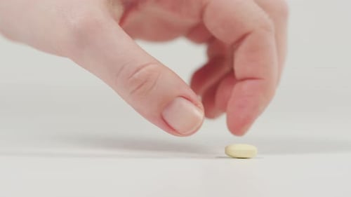 Hand Picking Up Small Yellow Pill Close Up