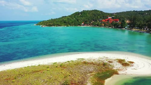 Calm turquoise sea, small sandbank with tropical vegetation and coast with hills and palms in the ba