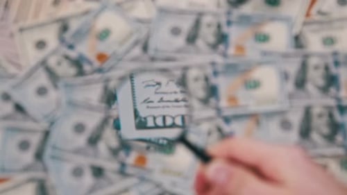Hand Inspecting Currency Through Magnifying Glass